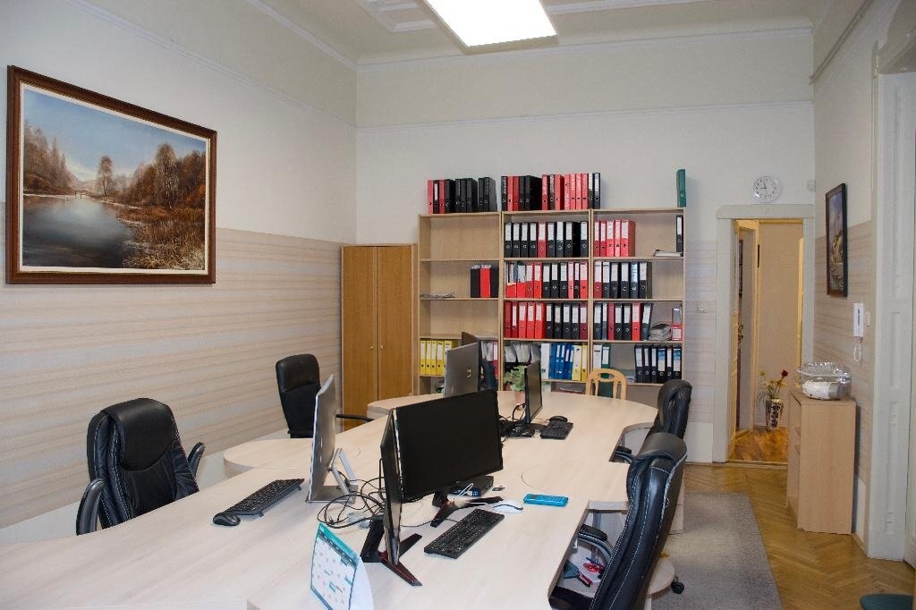 Tágas irodahelyiség nagy tárgyalóasztallal és irattároló polcokkal