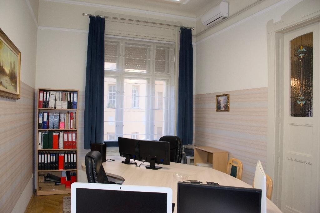 Világos tárgyalóterem nagy asztallal, könyvespolccal és klímával